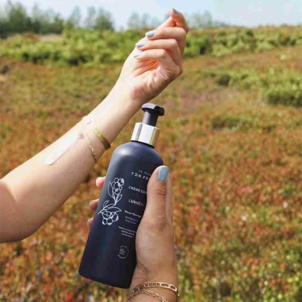Bouteille de Crème Corps Lumière au Bleuet Sauvage tenue en main dans un champ de bleuets