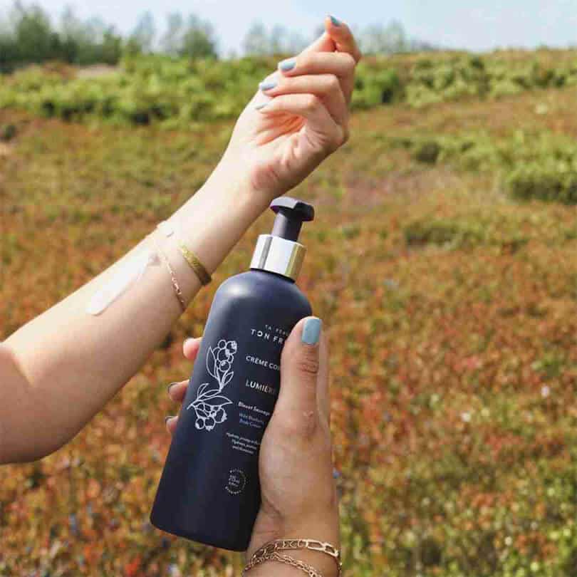 Bouteille de Crème Corps Lumière au Bleuet Sauvage tenue en main dans un champ de bleuets